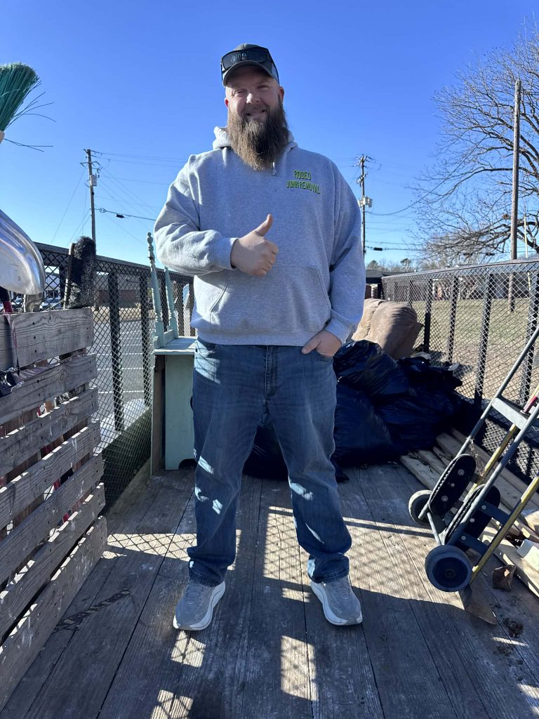Nick Breeden, owner of Rodeo Junk Removal, standing on the back of a trailer in uniform.